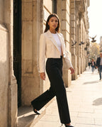 Blazer court beige Léontine, porté devant un immeuble en pierre calcaire au soleil