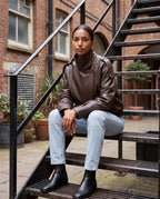 Blouson effet cuir marron Octavie, porté assis sur un escalier urbain