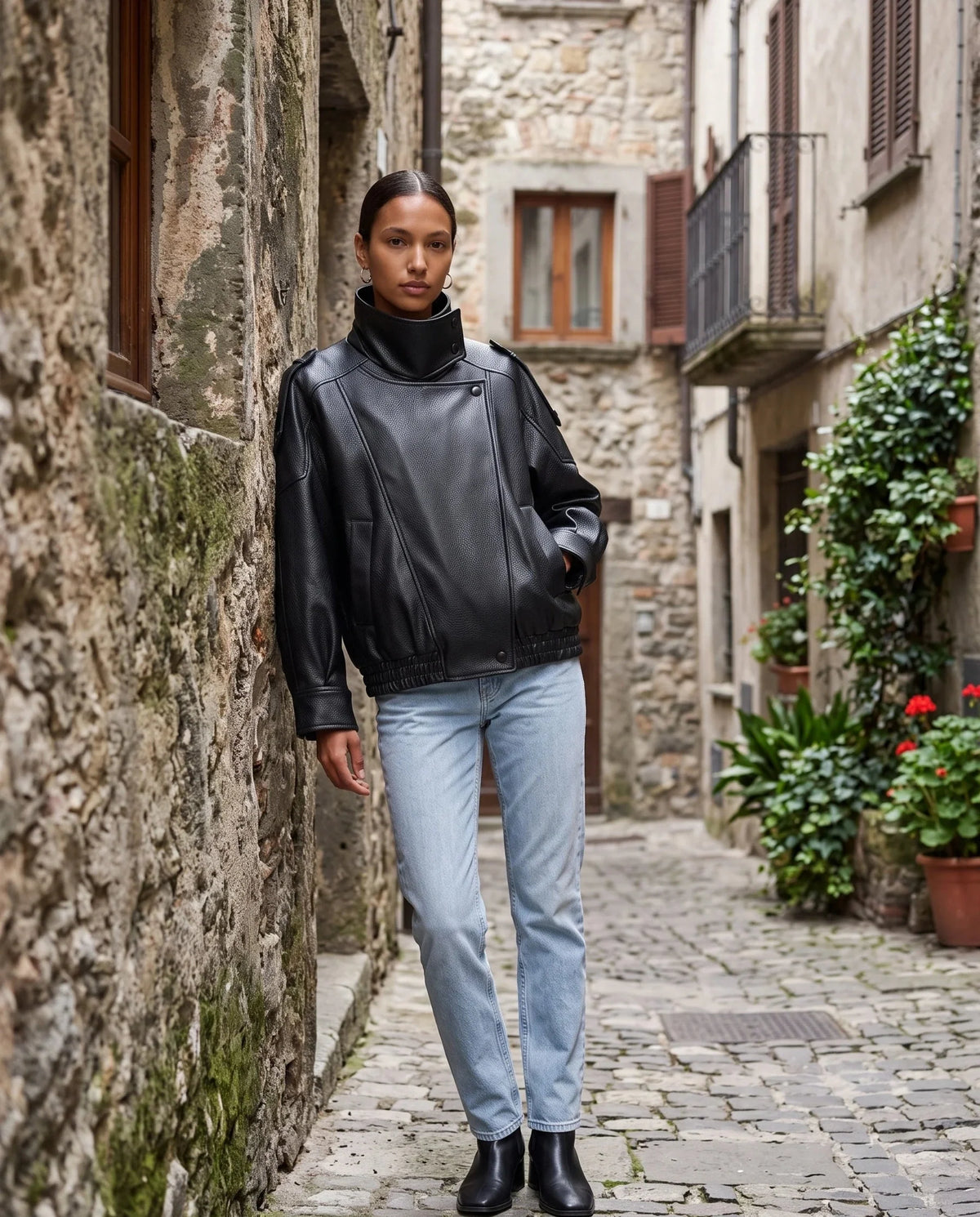 Blouson effet cuir noir Octavie, porté dans une ruelle en pierre