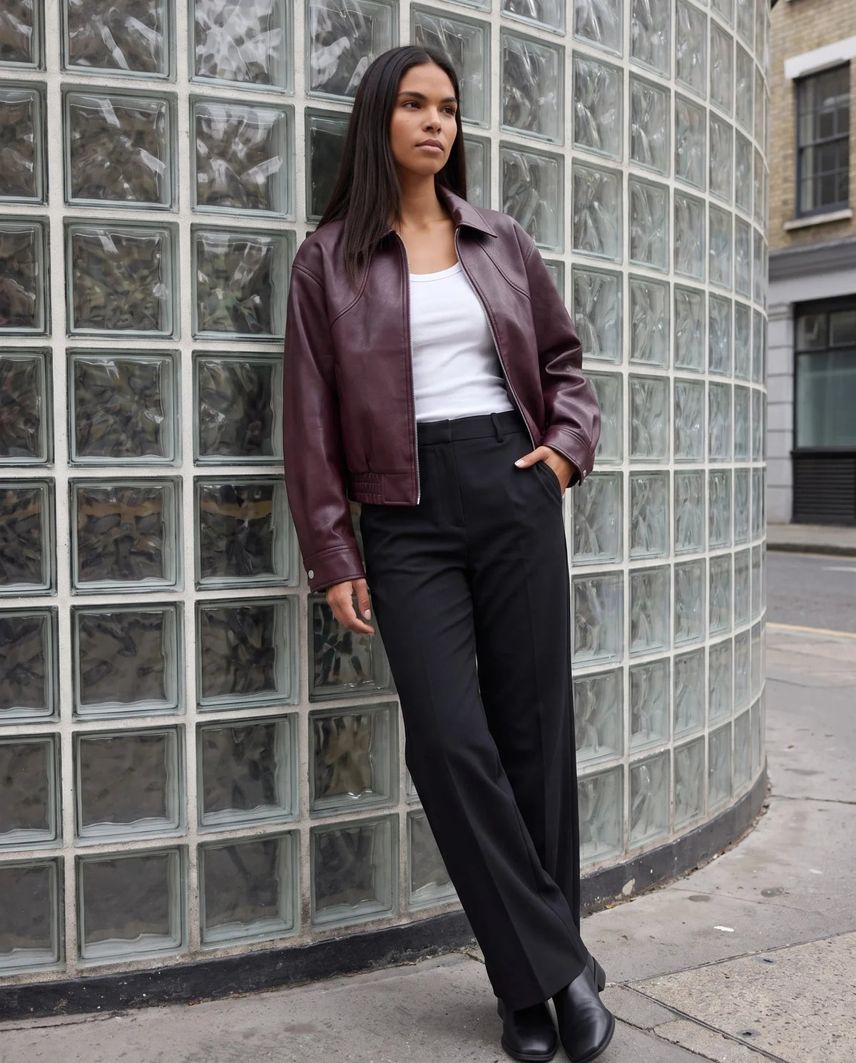 Blouson moto effet cuir lie de vin Philippine, porté devant un mur de briques de verre