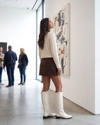 Bottes cavalières hautes effet cuir Bastienne — Blanc Cassé, portées dans une galerie d'art aux murs blancs