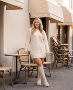 Bottes chaussettes hautes en maille Sylvette — Beige, portées à la terrasse d'un café aux stores écrus