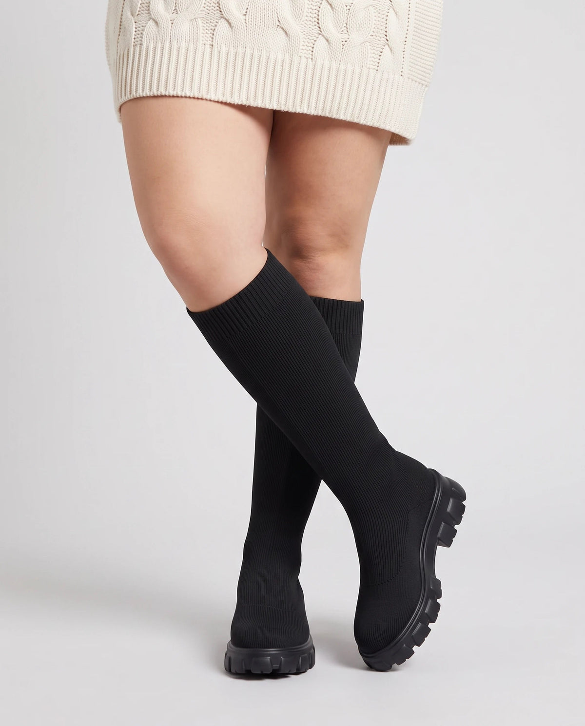 Bottes chaussettes hautes en maille Sylvette — Noir, portées en plan rapproché, chevilles croisées