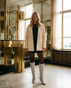 Bottes hautes à paillettes à talon aiguille Amarante — Argent, portées dans un hall Art déco aux miroirs