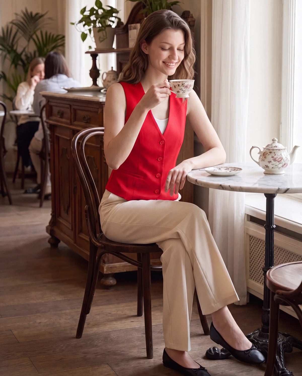 Gilet de tailleur rouge profond Bérénice, porté dans un salon de thé élégant