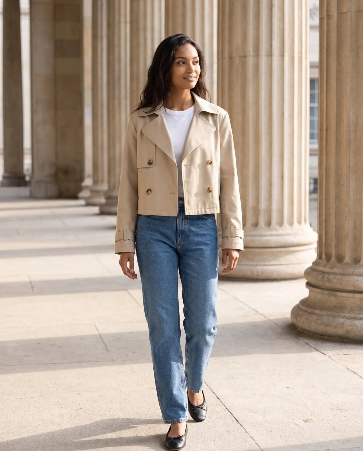 Trench court croisé beige Aliénor, porté sur une esplanade à colonnades
