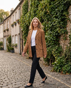 Veste-blazer en suédine marron Eugénie, portée le long d'un mur de lierre