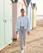 Veste zippée sans col bleu glacier Capucine, portée devant des cabines de plage pastel