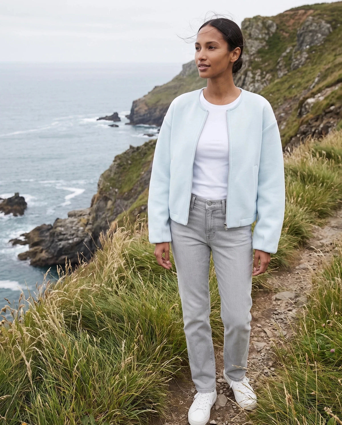 Veste zippée sans col bleu glacier Capucine, portée sur un sentier de falaise côtière