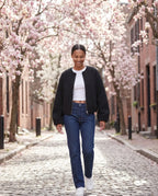 Veste zippée sans col noire Capucine, portée dans une allée de magnolias en fleurs