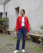 Veste zippée sans col rouge Capucine, portée dans une cour aux murs gris perle